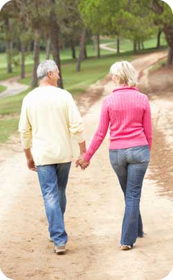 older married couple walking hand in hand through forest